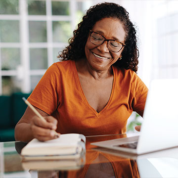 A woman smiling as she works on some paperwork on her computer. Links to Tangible Personal Property