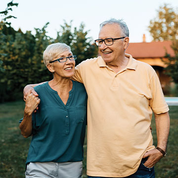 A man wraps his arm around his wife's shoulders as they take a stroll outdoors. Links to Gifts of Life Insurance